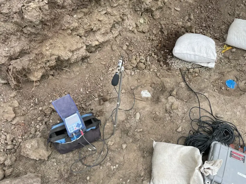 Instantel seismograph and microphone set up beside an excavation, with sandbagged sensors and cable